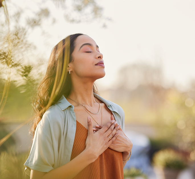 Woman with her hands over her heart standing outdoors in the morning sunlight
